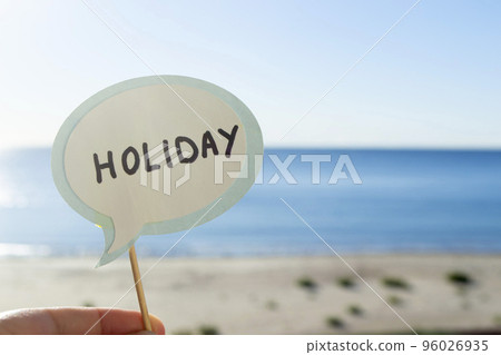 Stick with paper speech bubble with words Holiday on background blue sea, sky, sandy beach on sunny summer day. Text-balloons with text from letters. Concept, symbol, sign vacation travel tourism rest Stick with paper speech bubble with words Holiday on background blue sea, sky, sandy beach on sunny summer day. Text-balloons with text from letters. Concept, symbol, sign vacation travel tourism rest 96026935