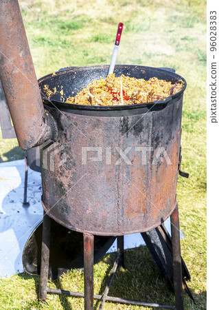 Cooking traditional Uzbek pilaf in a large cauldron 96028383