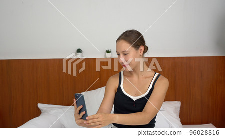 Happy caucasian woman using mobile phone taking selfie photo sitting on bed at home. Happy caucasian woman using mobile phone taking selfie photo sitting on bed at home. 96028816