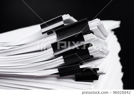 A stack of office papers, some of which are fastened with black binders 96028842