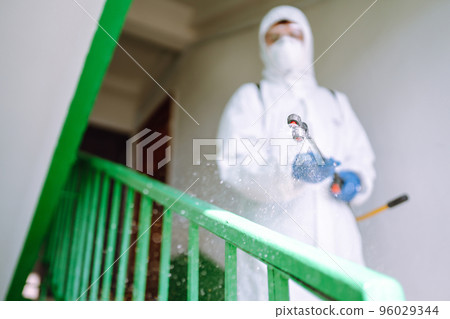 Man in Hazmat suit, protective gloves and goggles use sprayer equipment disinfect the entrance. Man in Hazmat suit, protective gloves and goggles use sprayer equipment disinfect the entrance. 96029344