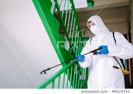 Man in Hazmat suit, protective gloves and goggles use sprayer equipment disinfect the entrance. 96029345