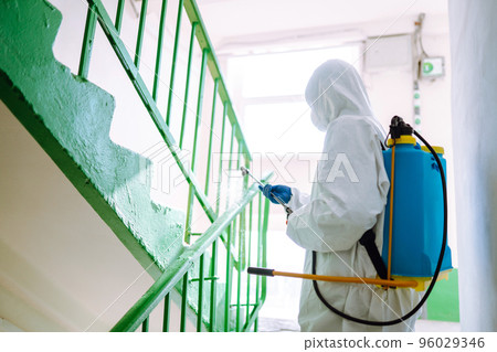 Man in Hazmat suit, protective gloves and goggles use sprayer equipment disinfect the entrance. Man in Hazmat suit, protective gloves and goggles use sprayer equipment disinfect the entrance. 96029346