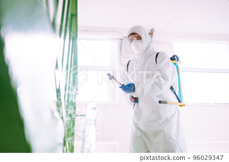 Man in Hazmat suit, protective gloves and goggles use sprayer equipment disinfect the entrance. Man in Hazmat suit, protective gloves and goggles use sprayer equipment disinfect the entrance. 96029347