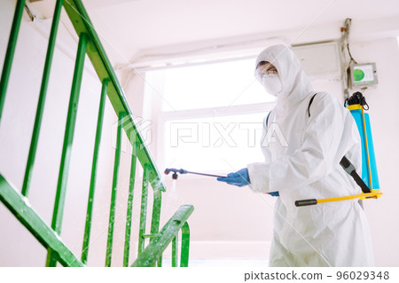 Man in Hazmat suit, protective gloves and goggles use sprayer equipment disinfect the entrance. Man in Hazmat suit, protective gloves and goggles use sprayer equipment disinfect the entrance. 96029348