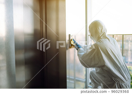 Cleaning and disinfection of the elevator to prevent COVID-19. Worker wearing protective suit sprays. Cleaning and disinfection of the elevator to prevent COVID-19. Worker wearing protective suit sprays. 96029368