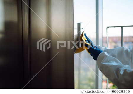 Cleaning and disinfection of the elevator to prevent COVID-19. Worker wearing protective suit sprays. Cleaning and disinfection of the elevator to prevent COVID-19. Worker wearing protective suit sprays. 96029369