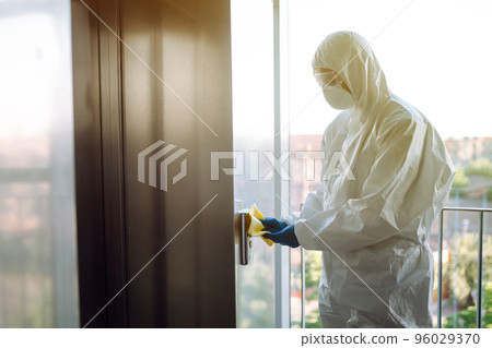 Cleaning and disinfection of the elevator to prevent COVID-19. Worker wearing protective suit sprays. Cleaning and disinfection of the elevator to prevent COVID-19. Worker wearing protective suit sprays. 96029370