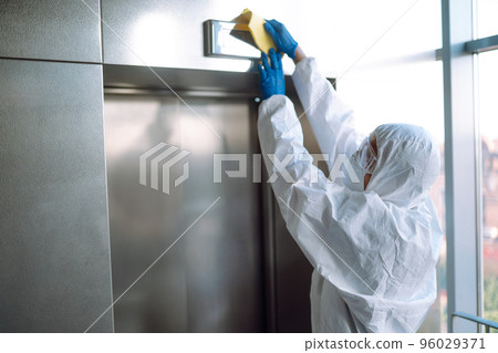 Cleaning and disinfection of the elevator to prevent COVID-19. Worker wearing protective suit sprays. Cleaning and disinfection of the elevator to prevent COVID-19. Worker wearing protective suit sprays. 96029371