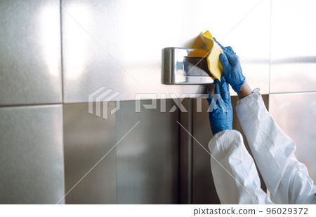 Cleaning and disinfection of the elevator to prevent COVID-19. Worker wearing protective suit sprays. 96029372
