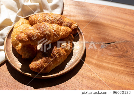 Croissant in wooden plate, white cloth, morning sunshine 96030123