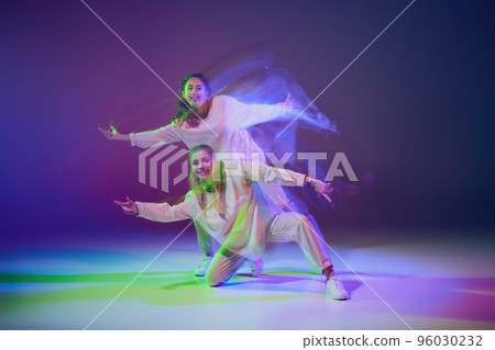Portrait of young girls dancing hip-hop isolated over gradient blue purple background in neon with mixed light. Happiness 96030232