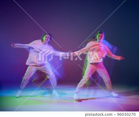 Portrait of young girls dancing hip-hop isolated over gradient blue purple background in neon with mixed light. Modern dance 96030270