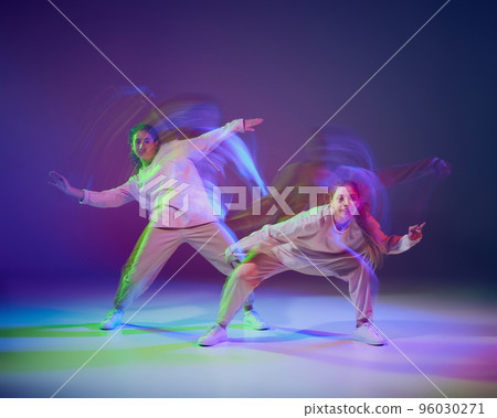 Portrait of young girls dancing hip-hop isolated over gradient blue purple background in neon with mixed light. Hobby 96030271