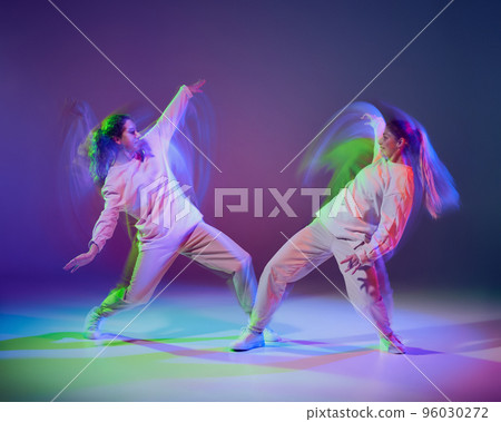 Portrait of young girls dancing hip-hop isolated over gradient blue purple background in neon with mixed light. Swag style 96030272
