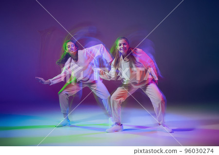 Portrait of young girls dancing hip-hop, contemp isolated over gradient blue purple background in neon with mixed light. 96030274