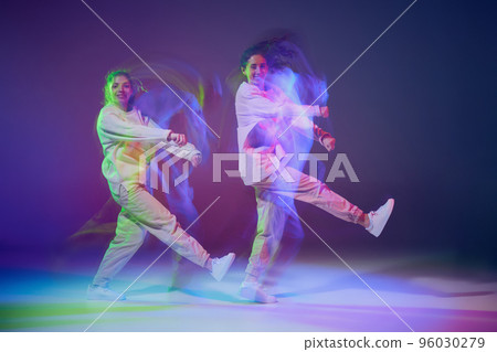 Portrait of young girls dancing hip-hop isolated over gradient blue purple background in neon with mixed light. Contemp dance 96030279