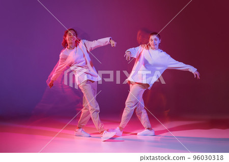 Portrait of two young girls dancing hip-hop isolated over gradient violet background in neon with mixed light. Casual look 96030318