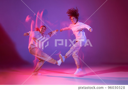 Portrait of cheerful young girls dancing hip-hop isolated over gradient purple background in neon with mixed light Portrait of cheerful young girls dancing hip-hop isolated over gradient purple background in neon with mixed light 96030328
