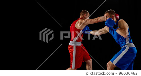 Male professional boxers in blue and red sports uniform practicing punch isolated on dark background. Concept of sport, competition, training, energy. Male professional boxers in blue and red sports uniform practicing punch isolated on dark background. Concept of sport, competition, training, energy. 96030462