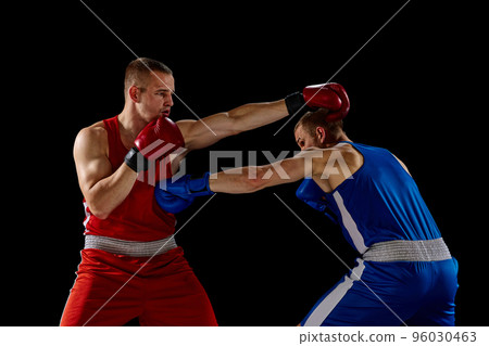 Male professional boxers in blue and red sports uniform practicing punch isolated on dark background. Concept of sport, competition, training, energy. 96030463