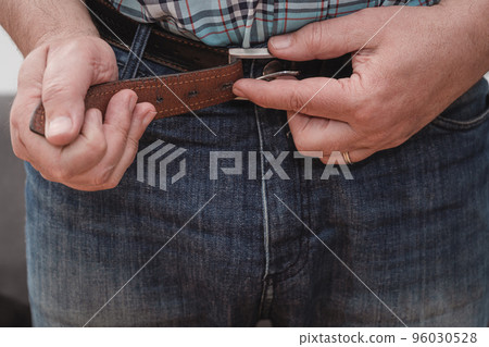 Close-up of a man's hands putting on a pair of jeans and closing the belt. 96030528