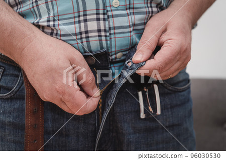 Close up man an trying to zipping his blue jeans pant. Close up man an trying to zipping his blue jeans pant. 96030530