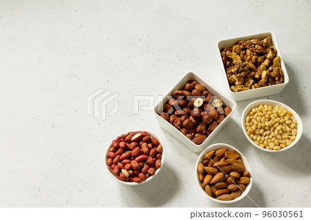 Various nuts in a ceramic bowl (walnut, almonds, pine nuts, hazelnuts) on a light stone table. The concept of a healthy dessert. Copy space. 96030561
