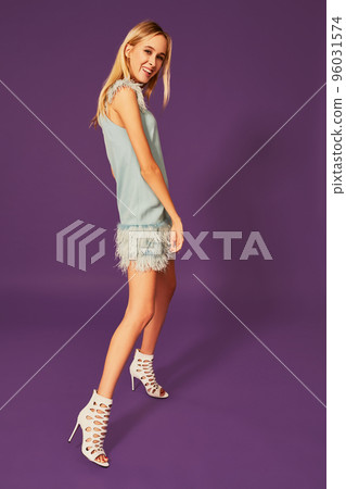 Image of cute beautiful slim blonde woman in elegant cocktail blue dress is posing at studio on purple background. 96031574
