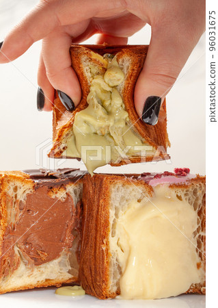 Female hand squeezing half of soft croissant cube with pistachio custard filling Female hand squeezing half of soft croissant cube with pistachio custard filling 96031675