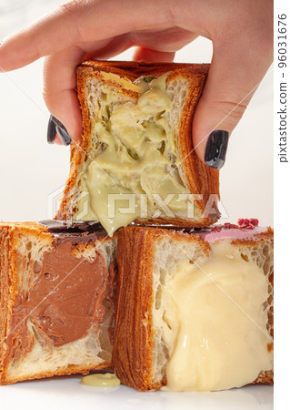 Female hand taking sliced fresh soft cube shaped croissant with pistachio custard Female hand taking sliced fresh soft cube shaped croissant with pistachio custard 96031676