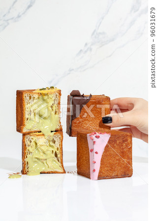 Female hand taking cube shaped croissant topped with ganache and chocolate chips Female hand taking cube shaped croissant topped with ganache and chocolate chips 96031679