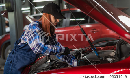 A woman auto mechanic in overalls is repairing a car. 96031949