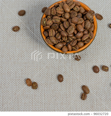 A cup with coffee beans on the background, spilled coffee beans near the cup. 96032720