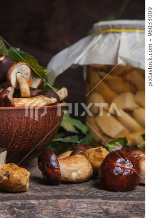Pile of Imleria Badia or Boletus badius mushrooms commonly known as the bay bolete with canned mushroom in glass jar on vintage wooden background.. 96033009