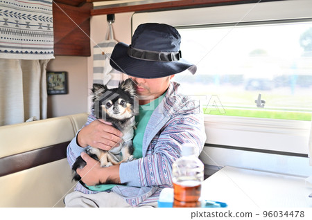 A man relaxing with a chihuahua in a camper 96034478