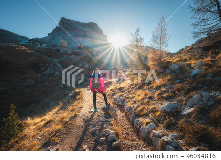 Walking girl with backpack on the trail in mountains at sunset Walking girl with backpack on the trail in mountains at sunset 96034816