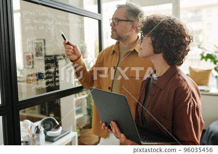 Young woman with laptop looking at notes on transparent board 96035456