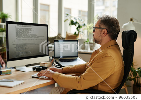 Serious mature software developer looking at code on screen 96035505