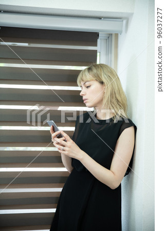 A woman looking at a smartphone with a serious face by the window 96037277