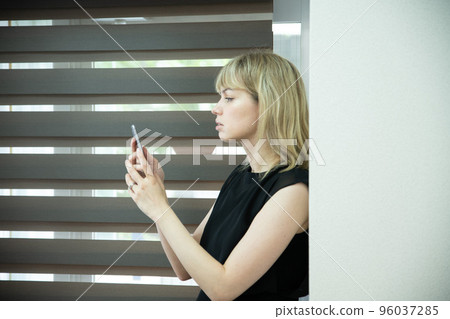 一個女人在窗邊看著一部嚴肅的智能手機 一個女人在窗邊看著一部嚴肅的智能手機 96037285
