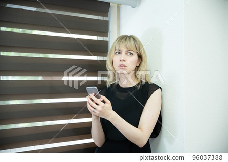 A woman looking at a smartphone with a serious face by the window 96037388