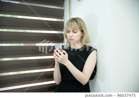 A woman looking at a smartphone with a serious face by the window A woman looking at a smartphone with a serious face by the window 96037475