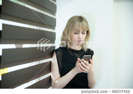 A woman looking at a smartphone with a serious face by the window 96037488