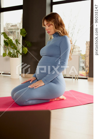 Portrait of young pregnant woman in sportswear sitting on yoga mat and meditating. Stretching exercises 96038147