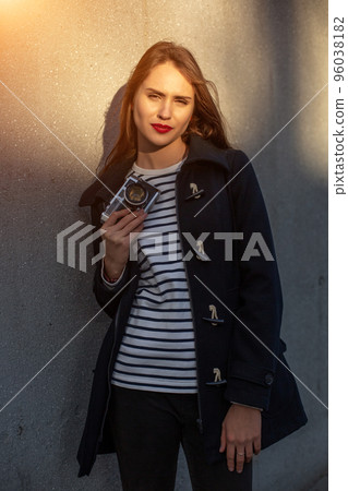 Smiling female photographer in jacket standing in front of wall ready to make new photo. Sun flare 96038182