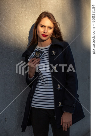 Smiling female photographer in jacket standing in front of wall ready to make new photo. Sun flare Smiling female photographer in jacket standing in front of wall ready to make new photo. Sun flare 96038184