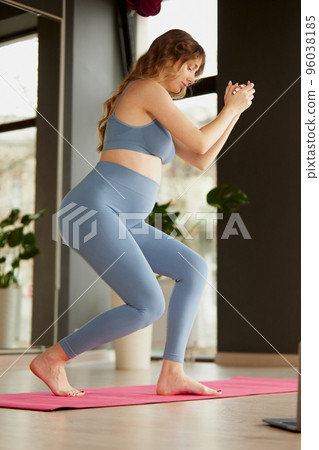 Portrait of young pregnant woman doing yoga with online lessons on laptop indoors on a daytime. Strength 96038185