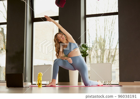 Portrait of young pregnant woman doing yoga with online lessons indoors on a daytime. Body stretching Portrait of young pregnant woman doing yoga with online lessons indoors on a daytime. Body stretching 96038191