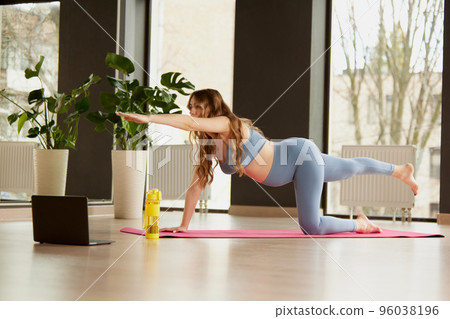 Portrait of young pregnant woman doing yoga on mat with online video lessons indoors on a daytime. Balance exercises Portrait of young pregnant woman doing yoga on mat with online video lessons indoors on a daytime. Balance exercises 96038196